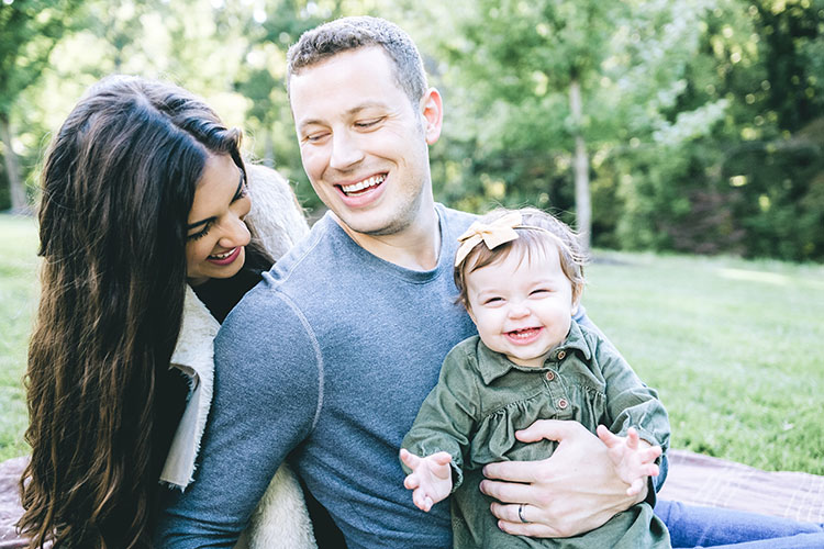 family photo of mom and dad with toddler girl wearing green dress