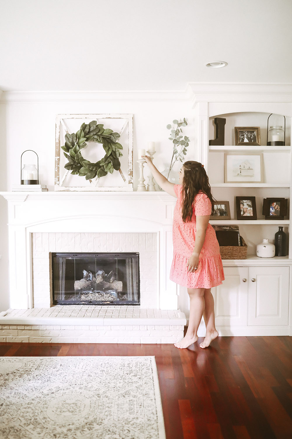 Neutral colored living room with white fireplace, mantle and built ins styled with frames, baskets, candles, and pops of greenery