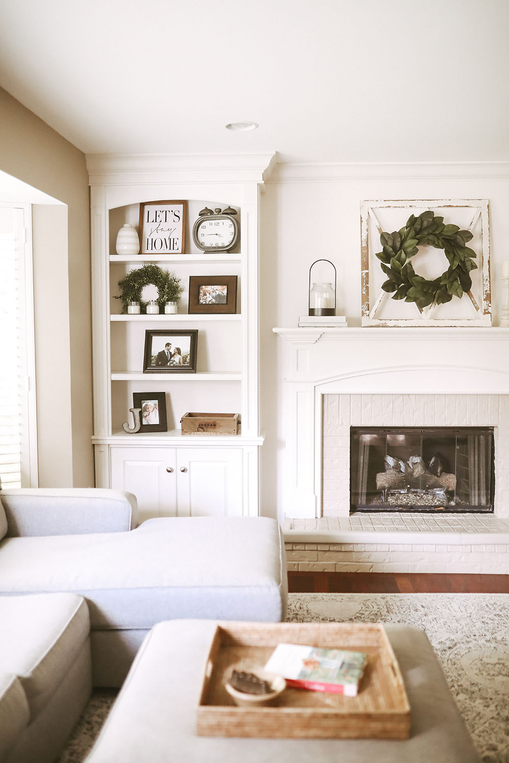 Neutral colored living room with white fireplace, mantle and built ins styled with frames, baskets, candles, and pops of greenery