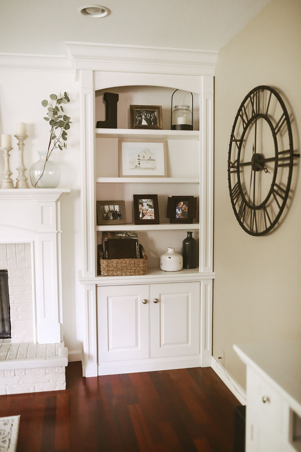 Neutral colored living room with white fireplace, mantle and built ins styled with frames, baskets, candles, and pops of greenery