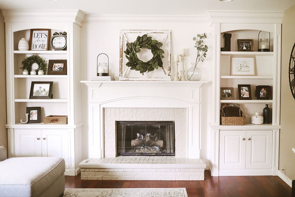 Neutral colored living room with white fireplace, mantle and built ins styled with frames, baskets, candles, and pops of greenery