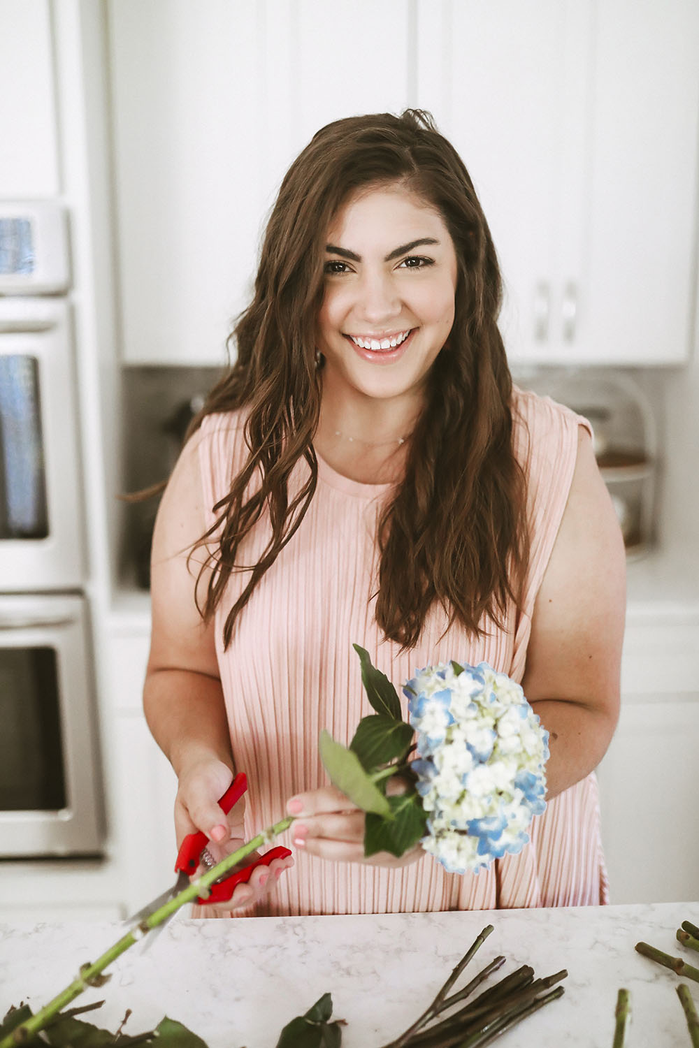 Woman wearing pink top holding floral scissors cutting blue hydrangeas