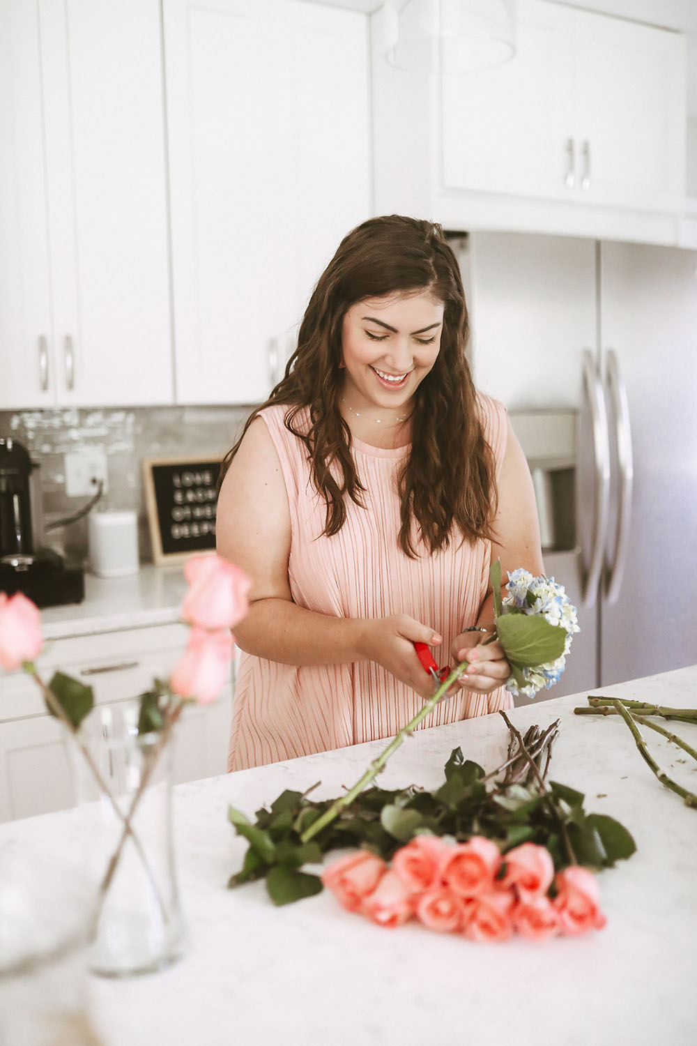 Woman wearing pink top holding floral scissors cutting blue hydrangeas and pink roses