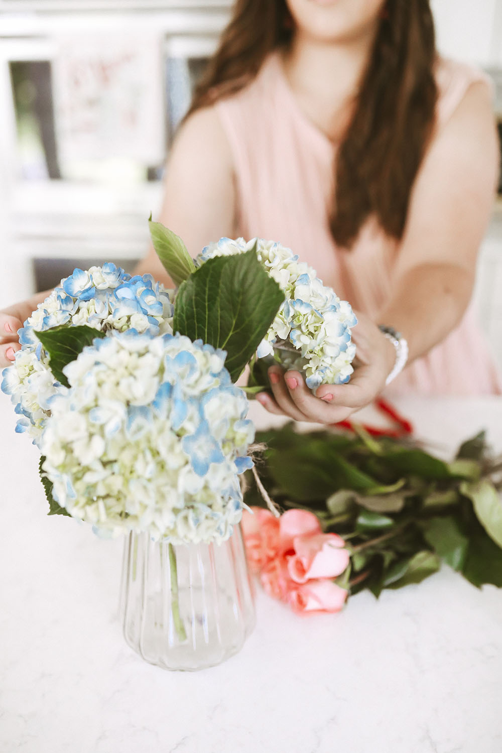 Woman wearing pink top styling blue hydrangeas in a vase