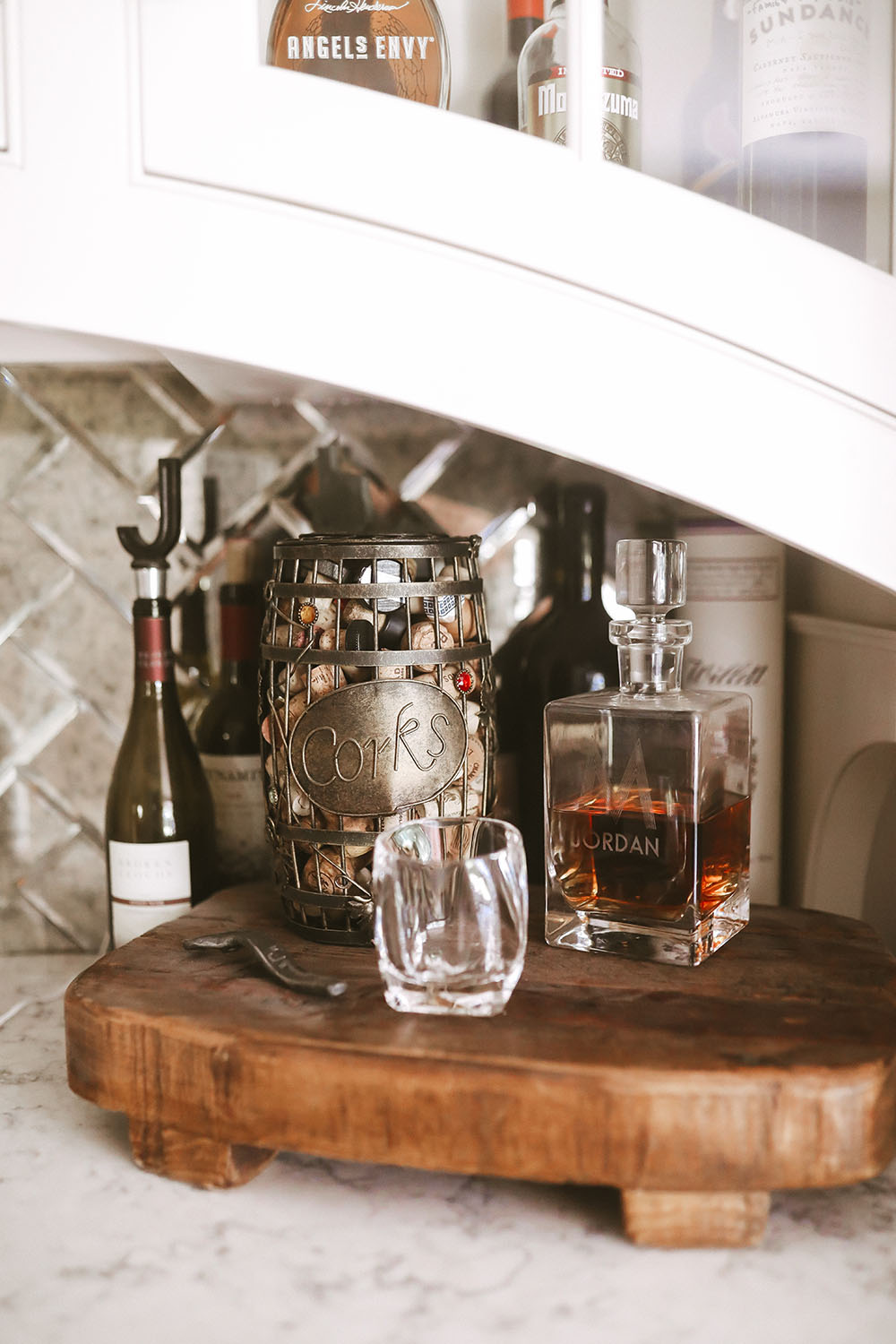 Wetbar showing wooden stand with decanter full of bourbon, basket holding corks, bottle opener and clear rocks glasses