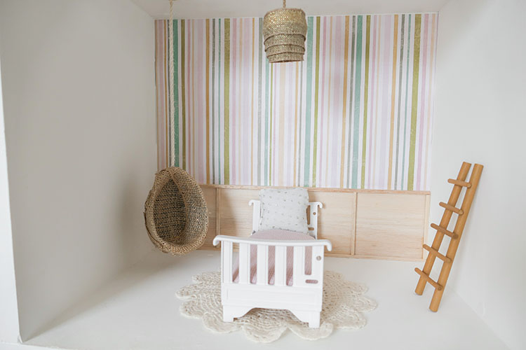 DIY dollhouse makeover project using a thrifted bookshelf showing bedroom with striped wallpaper, board and batten detail, hanging egg chair, bed, and ladder.