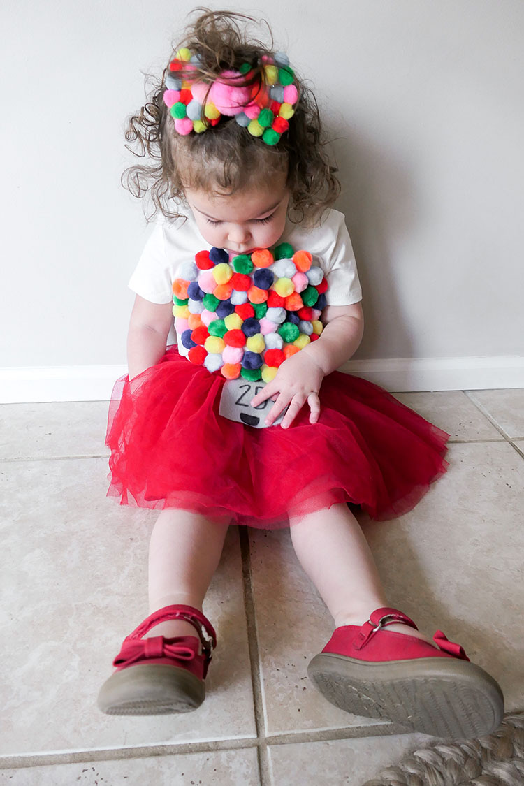 Toddler girl in diy gumball machine costume with red tutu and pom pom bow