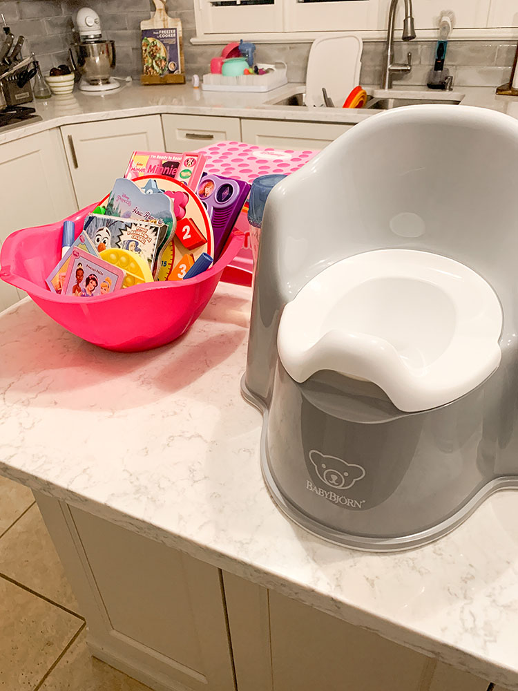 Potty training essentials of a small potty, basket of new goodies, and step stool.