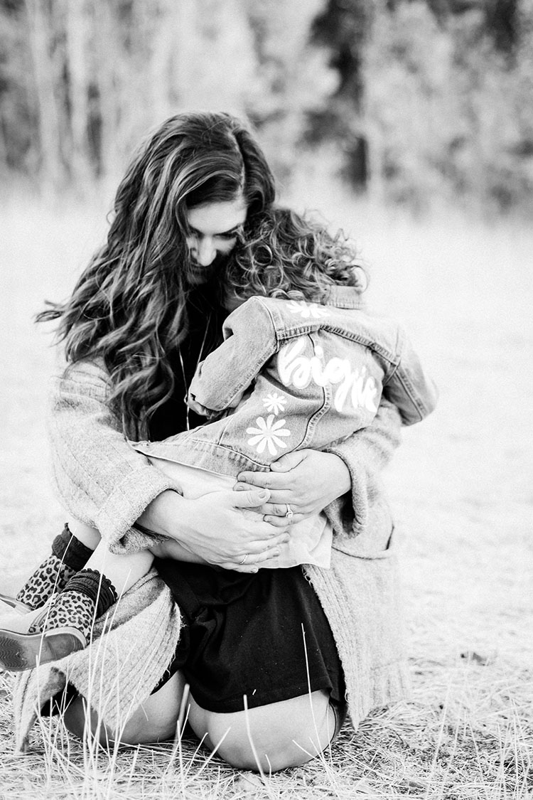 Little girl wearing jean jacket that says "big sis" on the back snuggling with mom