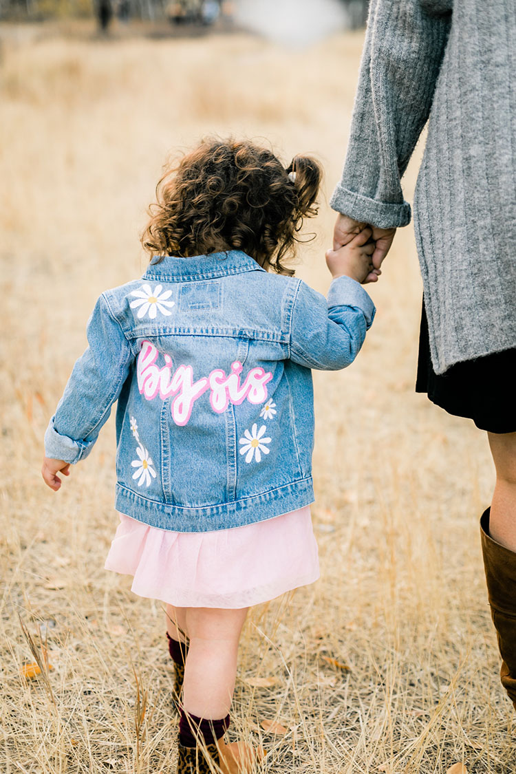 Little girl wearing custom denim jacket that reads "big sis" on the back.