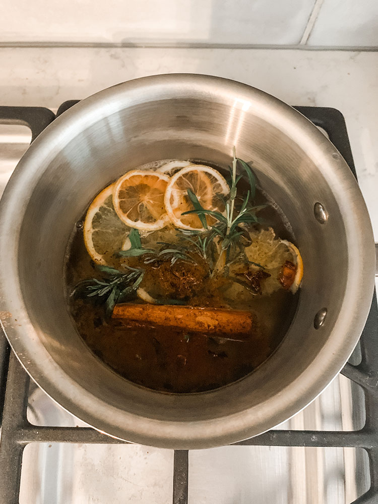 Large pot full of simmer pot ingredients such as dried citrus, rosemary, cinnamon sticks, and spices