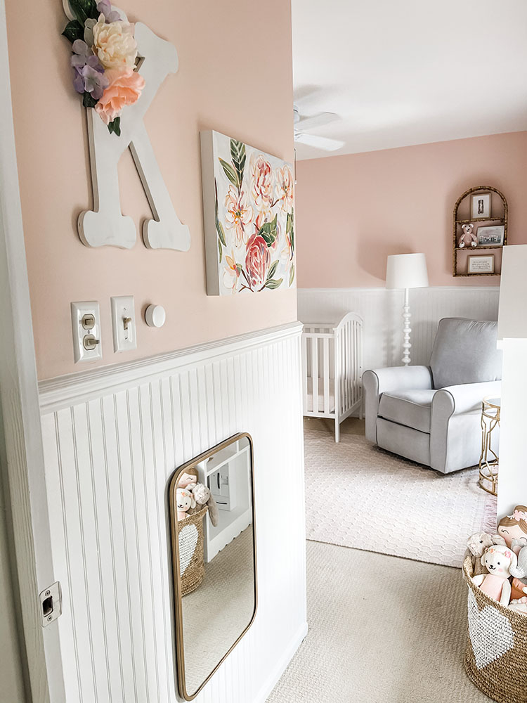 Walking into little girl's pink and white bedroom with white beadboard, wicker and white elements, pink rug and grey pottery barn glider