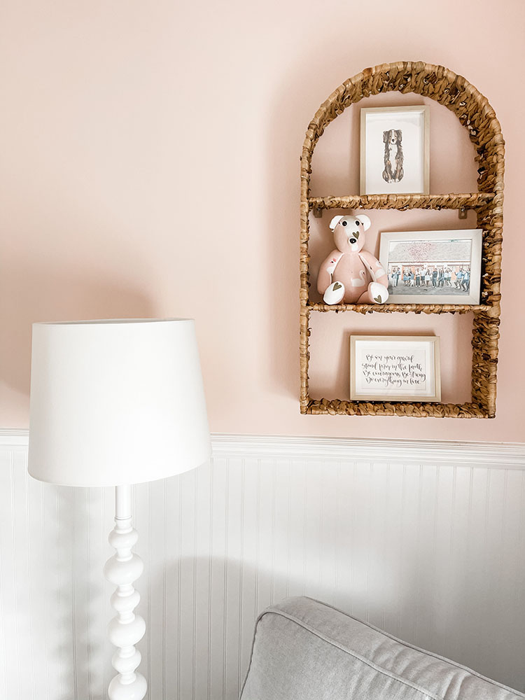 Little girl's pink and white bedroom showing wicker shelf that has pictures of family and a small pink bear on them