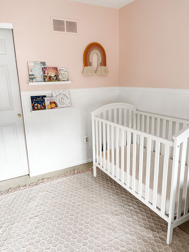 Little girl's pink and white bedroom with white shelves on the wall for books and macrame rainbow art