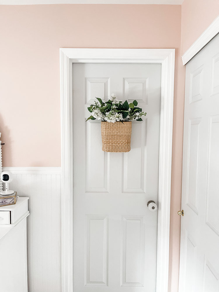 Little girl's pink and white bedroom showing door with basket of flowers hanging from it