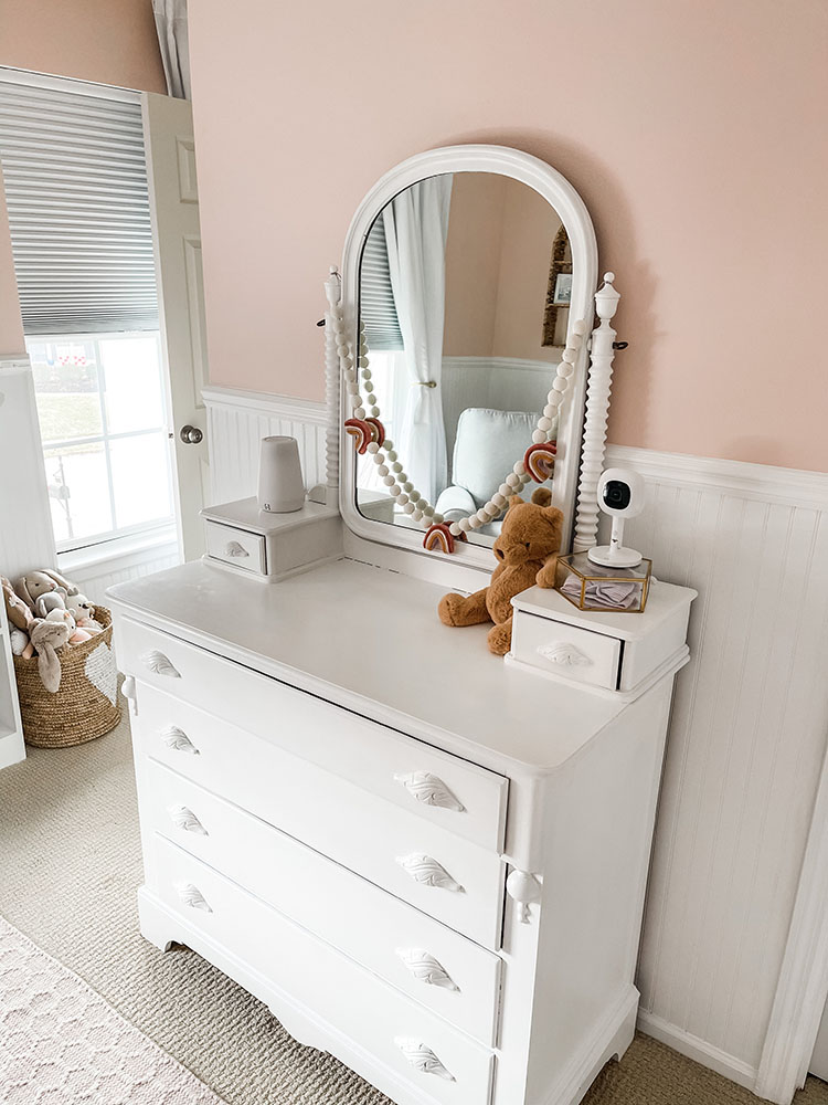 Little girl's pink and white bedroom showing white dresser with bear on top.