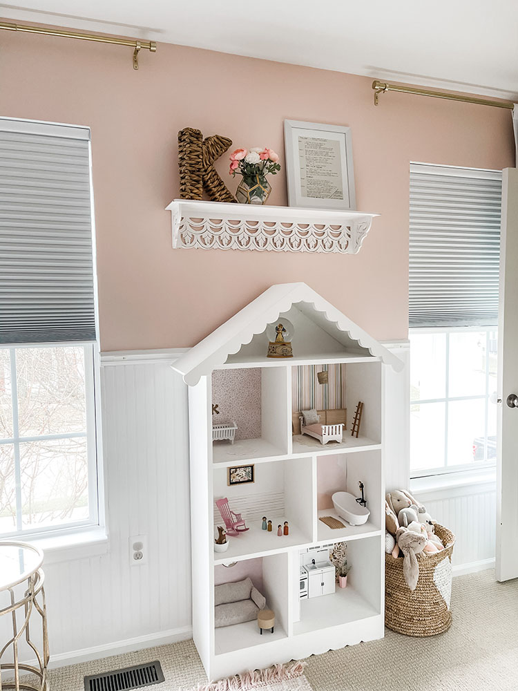 Little girl's pink and white bedroom showing large white dollhouse full of mini furniture, dolls, and decor