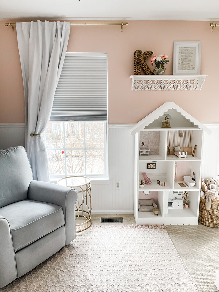 Pink and white toddler girl's room showing large white dollhouse against one of the walls next to a grey pottery barn glider