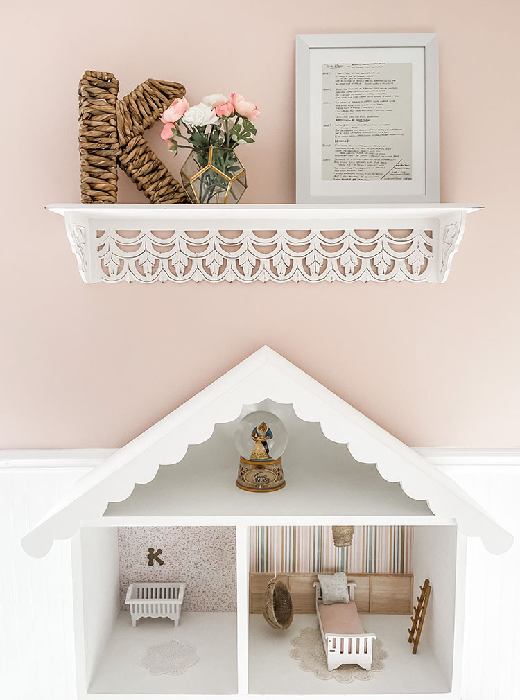 Little girl's pink and white bedroom showing dollhouse and white shelf