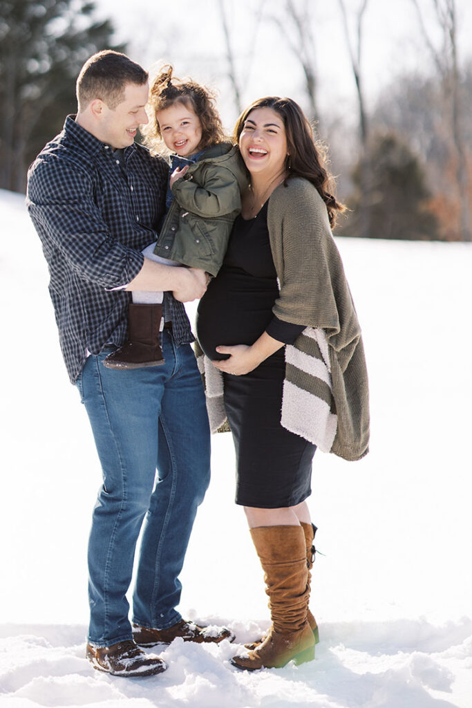 Dad, pregnant mom and toddler girl posing in the snow