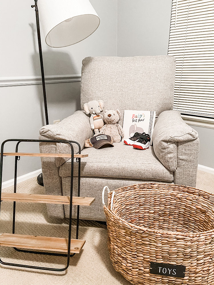 Baby boy's room showing grey Pottery Barn chair, stuffed bear and elephant, baby book, wood and iron shelf and wicker basket.