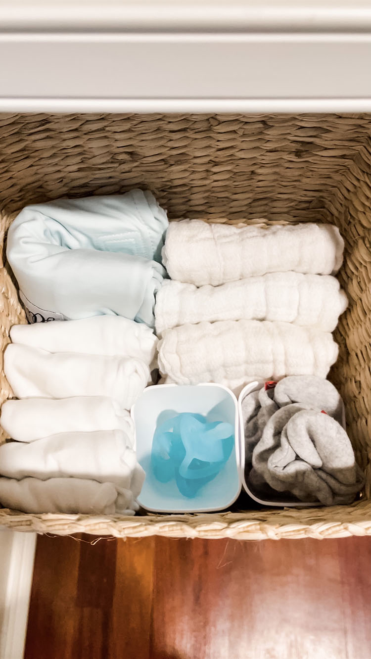 Basket with ollie swaddle, extra onesies, burp cloths, pacifiers, and booties for baby