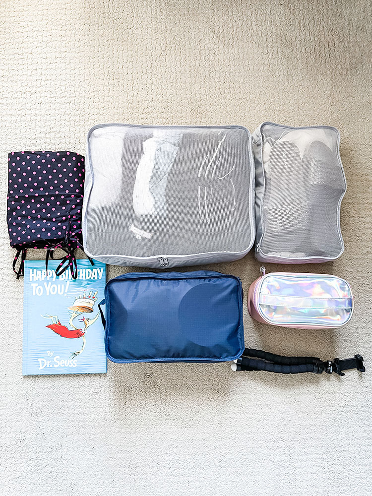 Polka dot birthing gown, two grey packing cubes, Dr. Seuss book, blue packing cube, pink toiletry bag, and mini tripod.