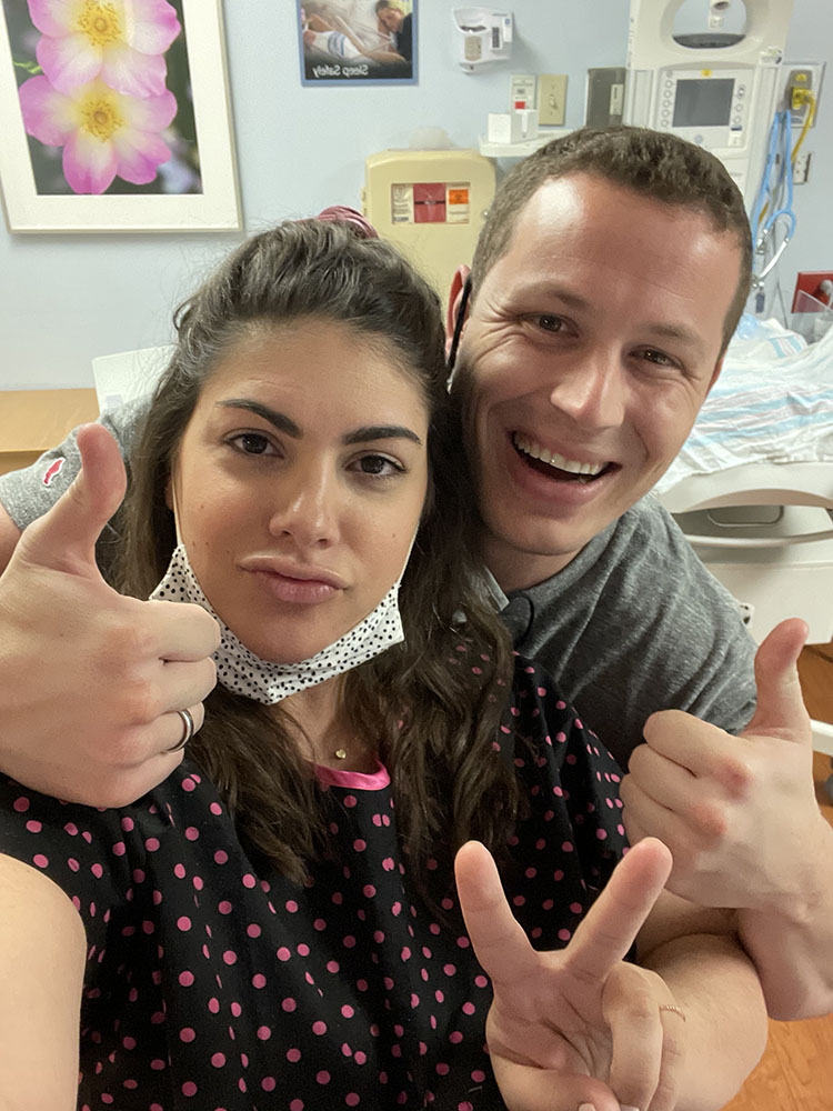 Laboring mom in polka dot birthing gown and husband giving thumbs up in the hospital