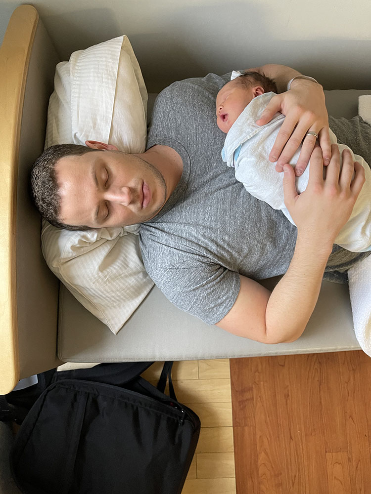 Dad asleep holding newborn baby boy in the hospital