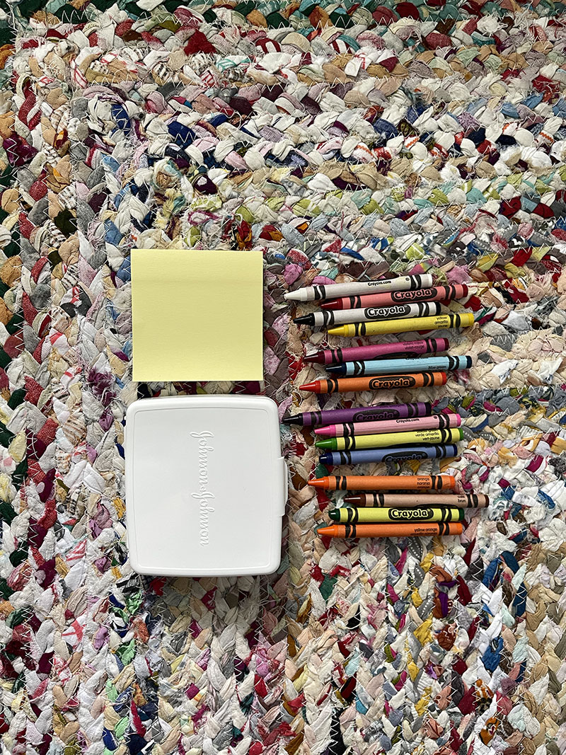 Post it notes, crayons and small white box all laying on a bright and colorful rug.