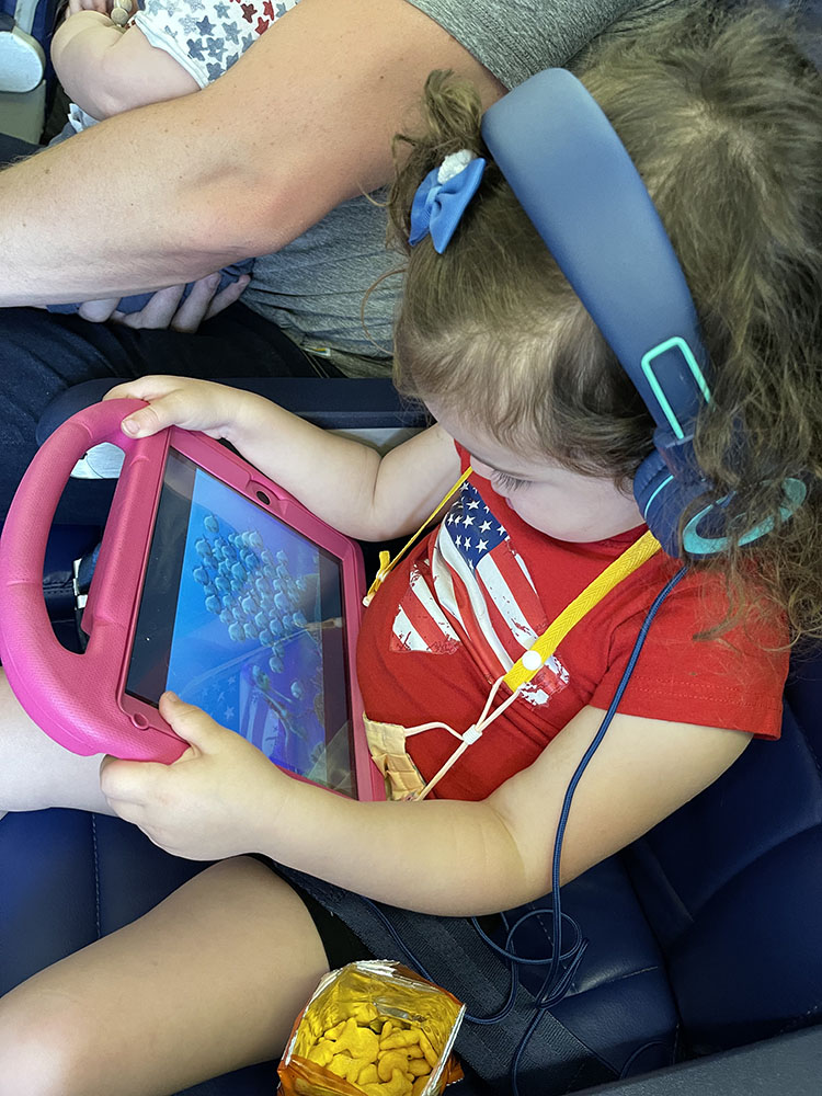 Little girl watching iPad with blue headphones while riding on an airplane.