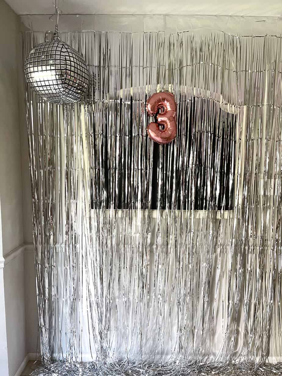 Metallic fringe photo backdrop with disco ball balloon and rose gold #3 balloon hanging.