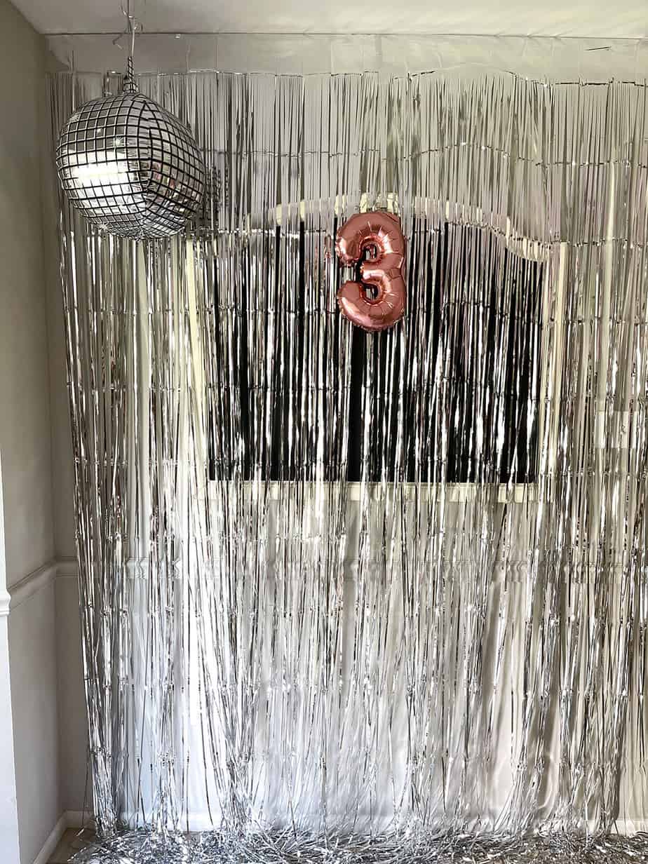 Metallic fringe photo backdrop with disco ball balloon and rose gold #3 balloon hanging.