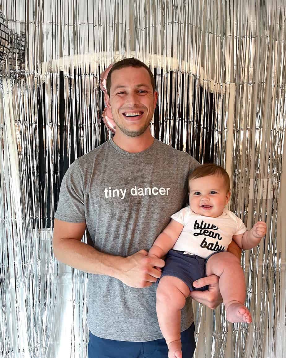 Metallic fringe photo backdrop with father and son wearing Elton John themed tshirts reading "tiny dancer" and "blue jean baby".