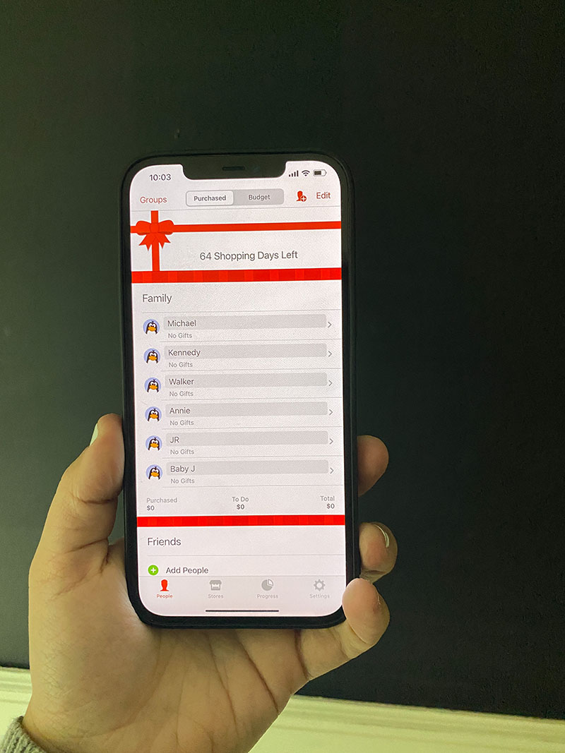 Holding an iPhone showing the Christmas List app where you can track gift items, budgets, what you've spent, wrapped, and more.