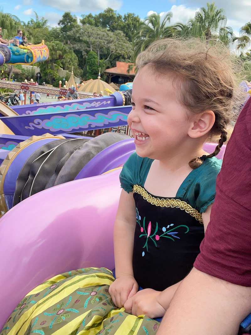 Little girl riding Aladdin Magic Carpets at Disney World while wearing a Princess Anna dress.