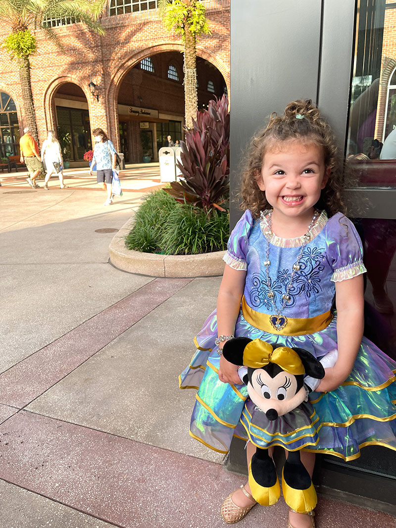 Little girl in Disney World's 50th Anniversary special Minnie Mouse dress holding Minnie Mouse doll at Disney Springs.