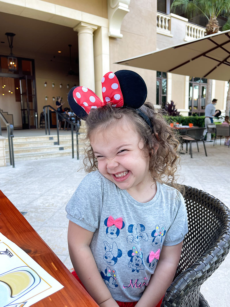 Little girl smiling while wearing Minnie Mouse tshirt and Minnie ears.