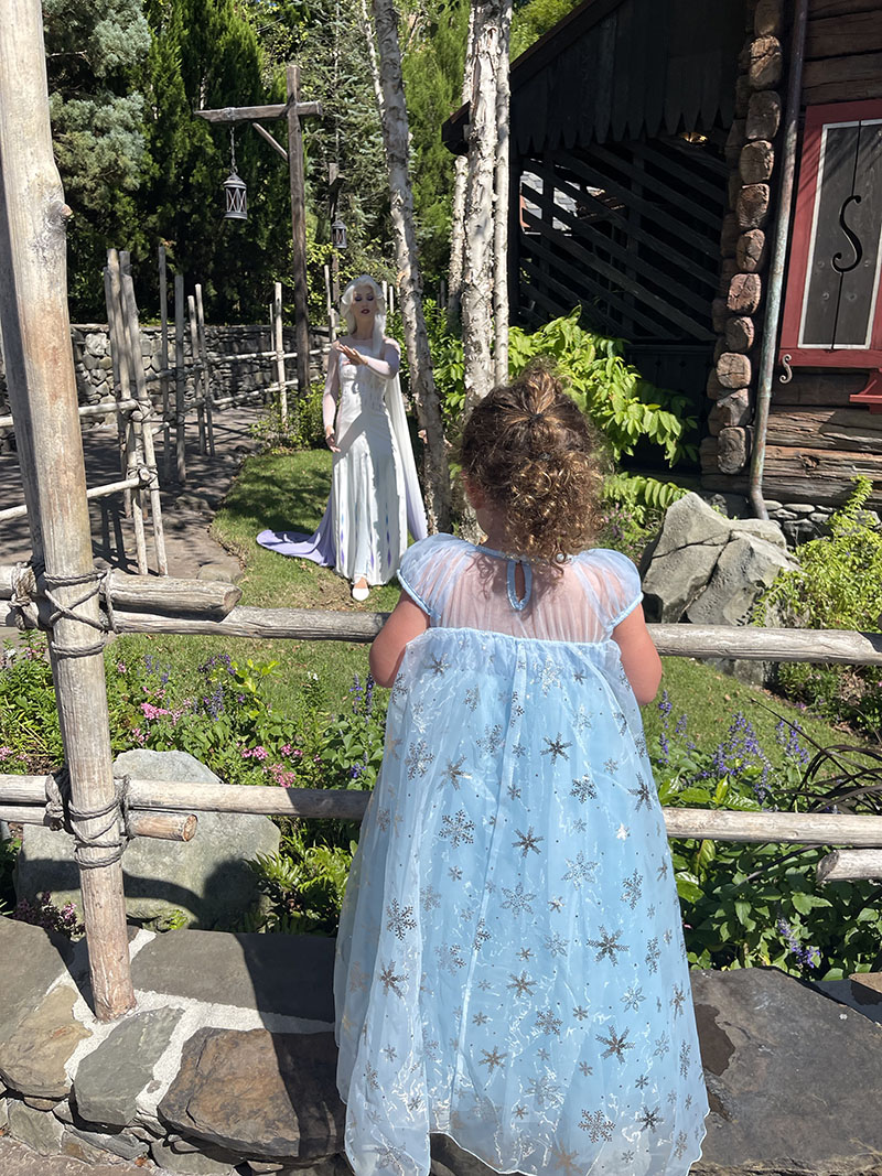 Little girl dressed in Queen Elsa blue dress with her back turned as she faces Queen Anna at Epcot in Florida.