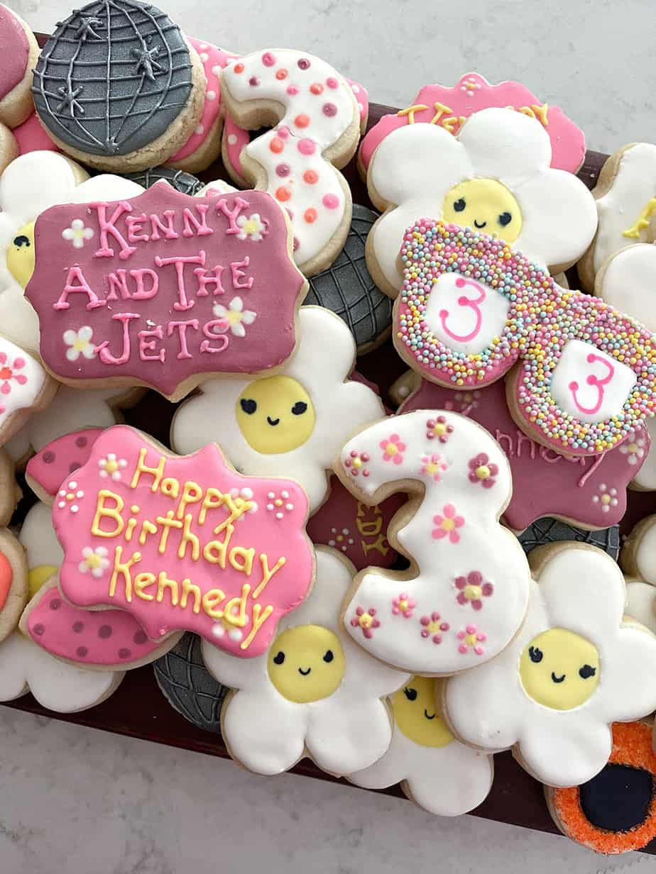 Custom cookies for 70s themed party with daisies, sunglasses, disco balls, and number three in pink, white, yellow, orange, and sprinkles.