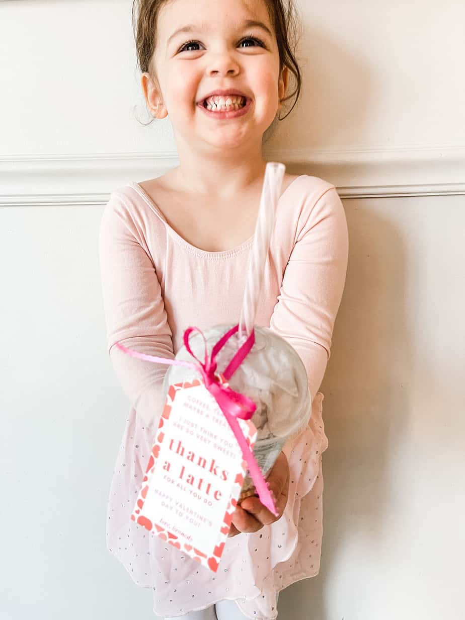 Little girl holding clear coffee cup filled with chocolates and a gift card with tag tied on saying "thanks a latte".