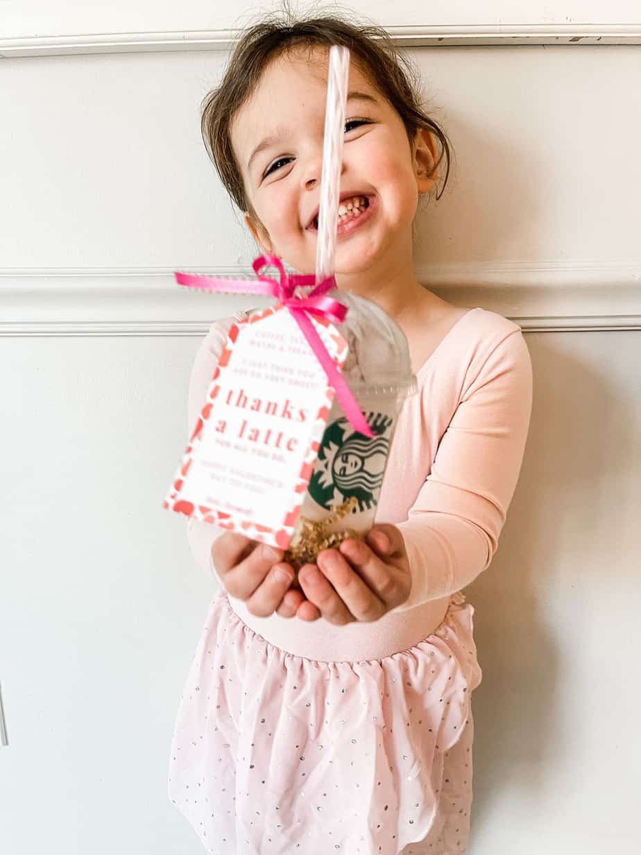 Little girl holding clear coffee cup filled with chocolates and a gift card with tag tied on saying "thanks a latte"