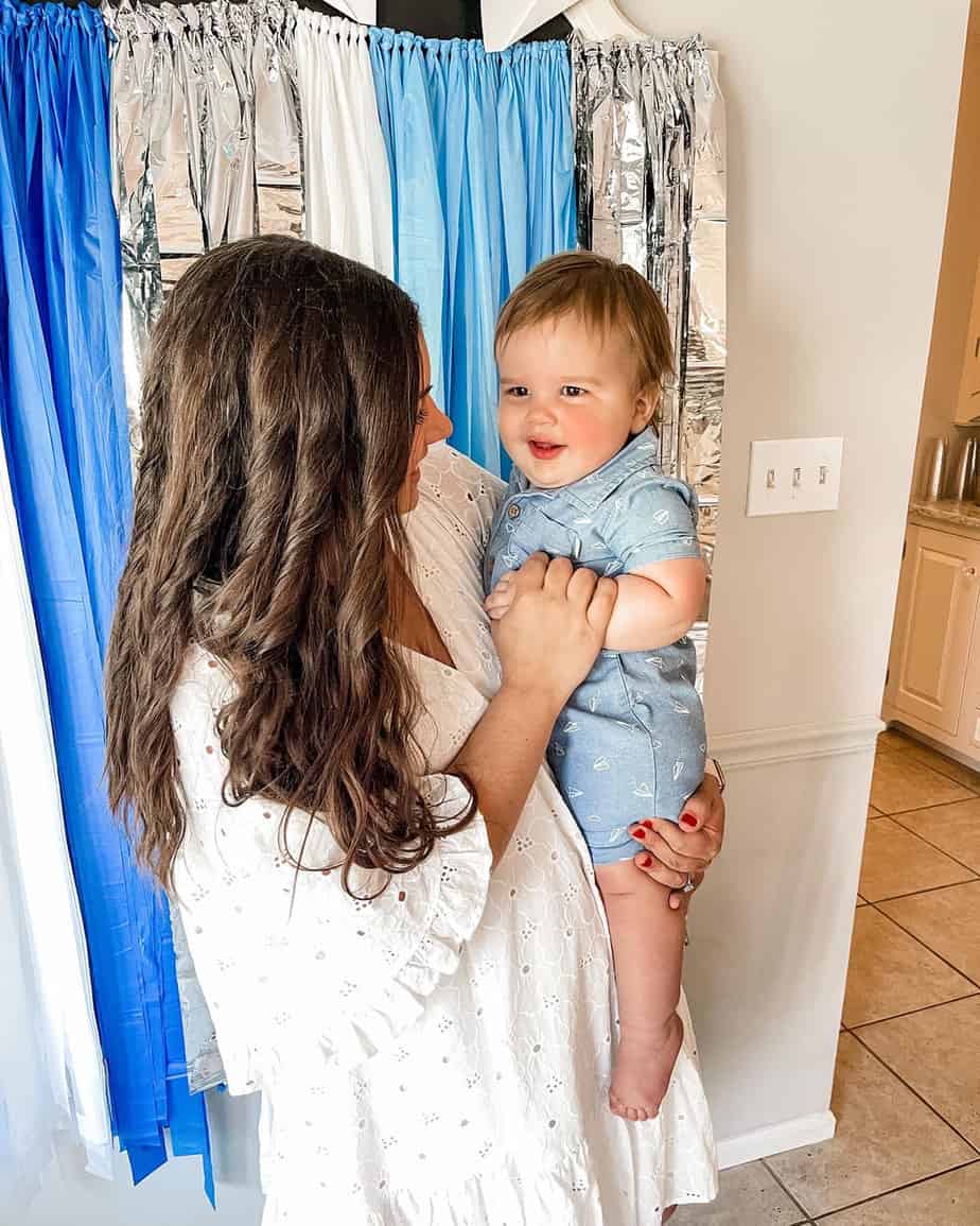 Mom wearing white dress holding little boy in front of blue backdrop