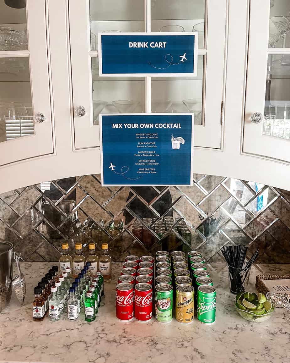 Drink cart set up for airplane themed party with mini soda cans, lime wedges, juice boxes, and small alcohol bottles