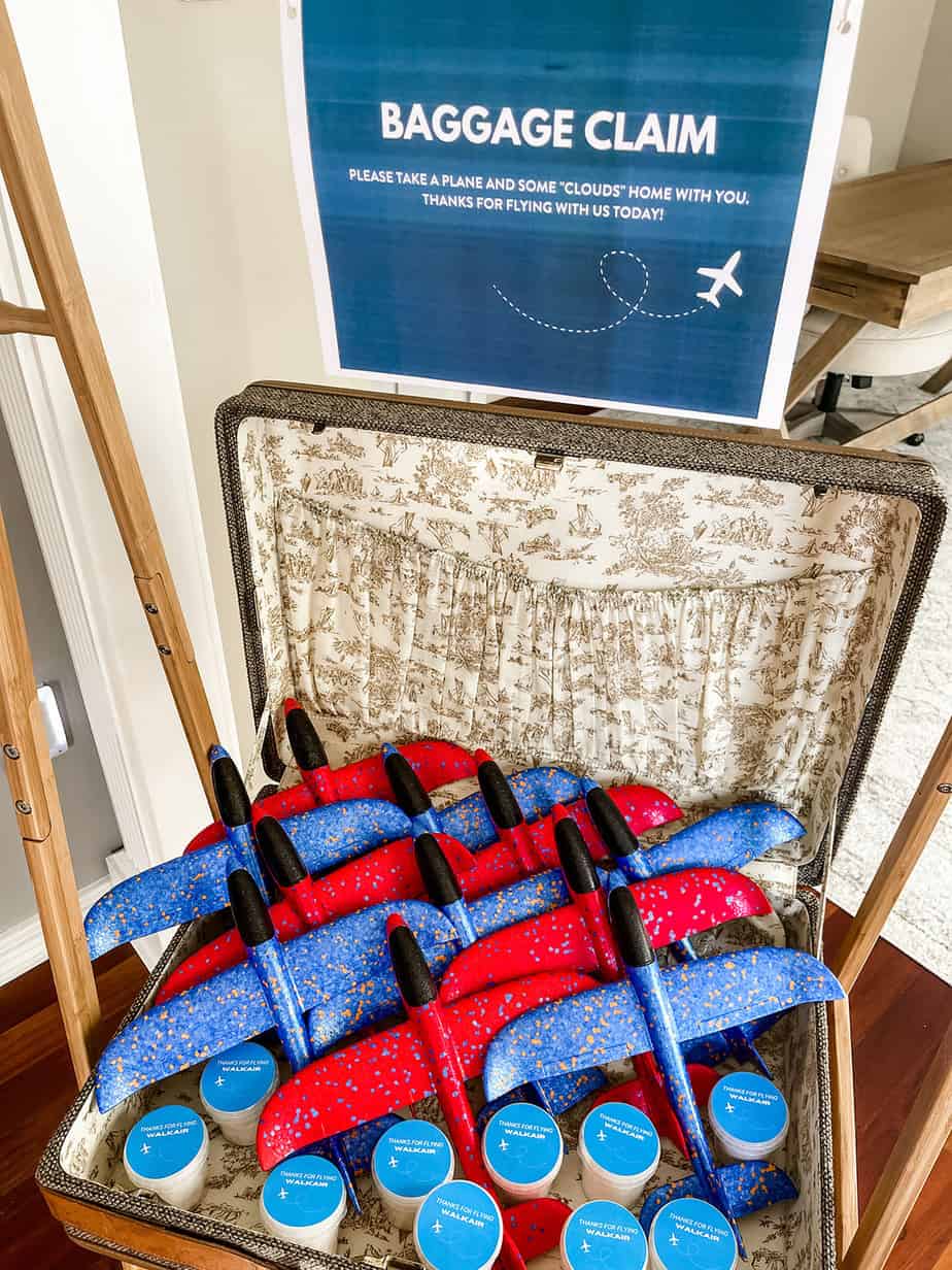 Suitcase full of blue and red foam airplanes and mini tubs of cotton candy for airplane party favors