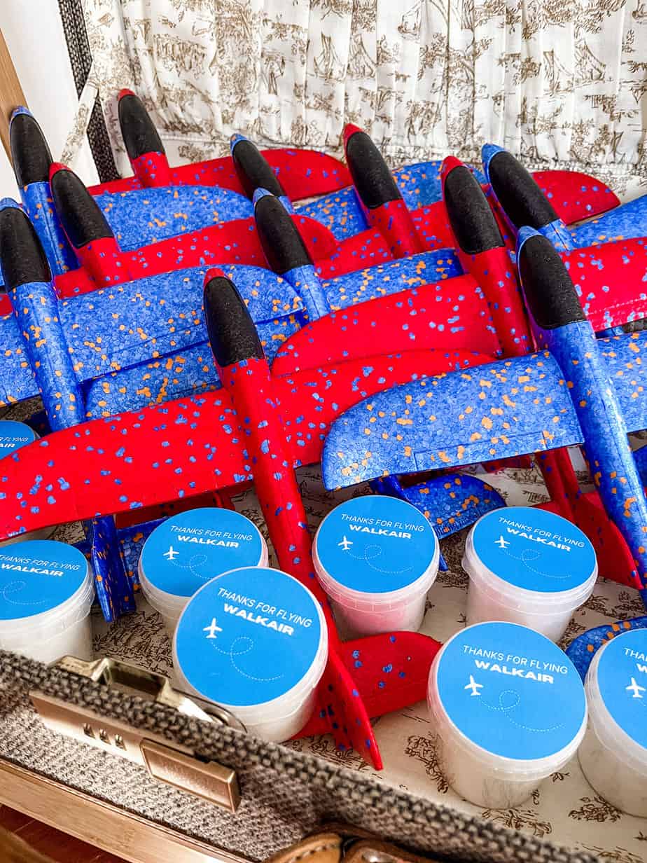Suitcase full of blue and red foam airplanes and mini tubs of cotton candy for airplane party favors