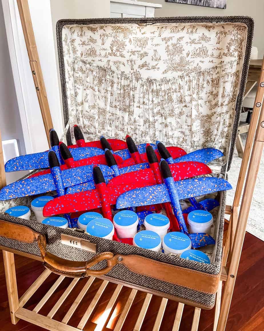 Suitcase full of blue and red foam airplanes and mini tubs of cotton candy for airplane party favors