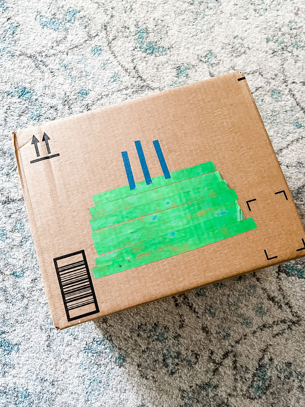 Green and blue washi tape in the shape of a birthday cake on a brown cardboard box.