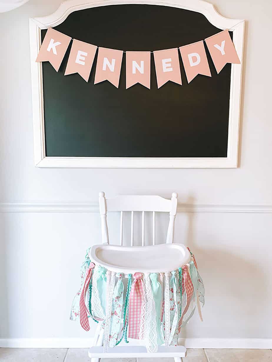 DIY high chair banner made of pink, blue and white strips of fabric tied to a white antique style high chair.