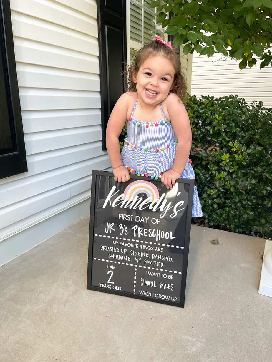 little girl in blue dress holding first day of school sign up before preschool